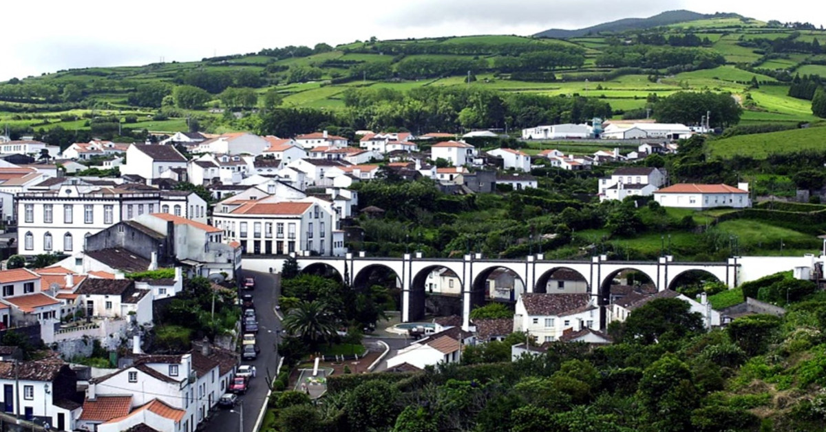Vista para uma vila açoriana com uma ponte branca e uma paisagem verdejante circundante